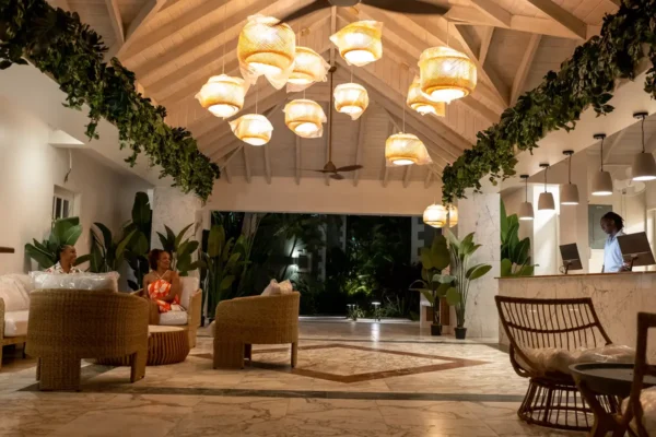 Warmly lit hotel lobby with rattan chairs, tropical greenery, and hanging lights at night at South Point Hotel Barbados