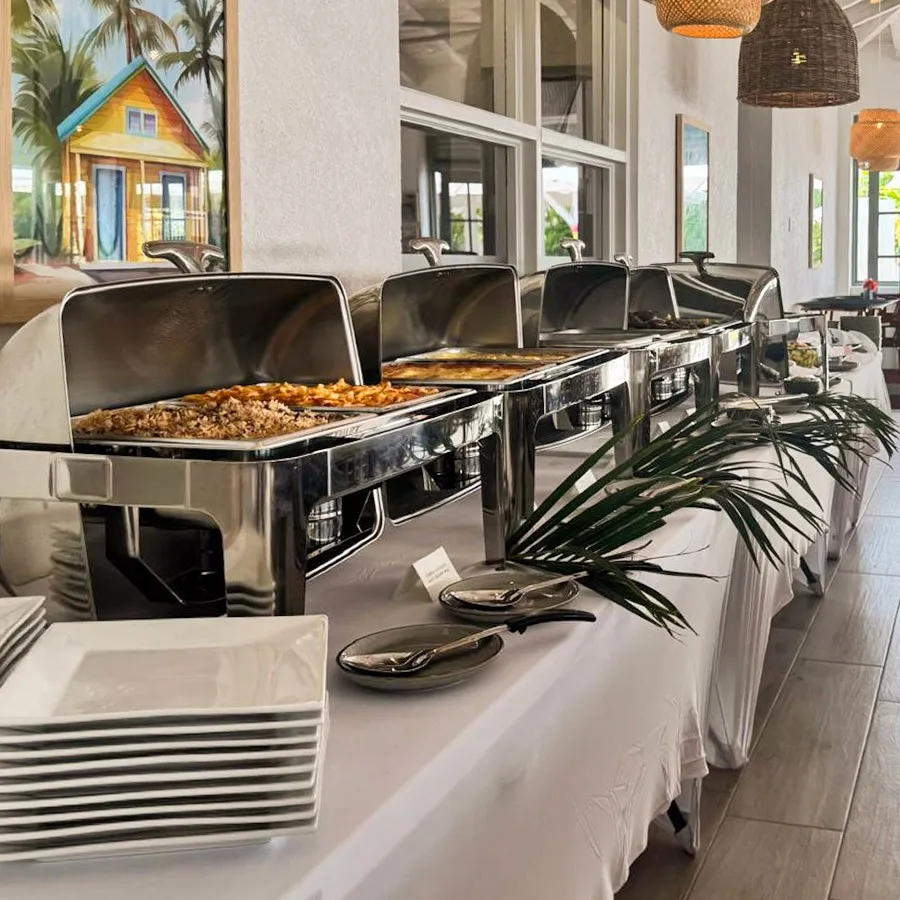 Buffet setup with chafing dishes filled with food, plates and serving utensils on a long table with a white tablecloth at Driftwood Restaurant.
