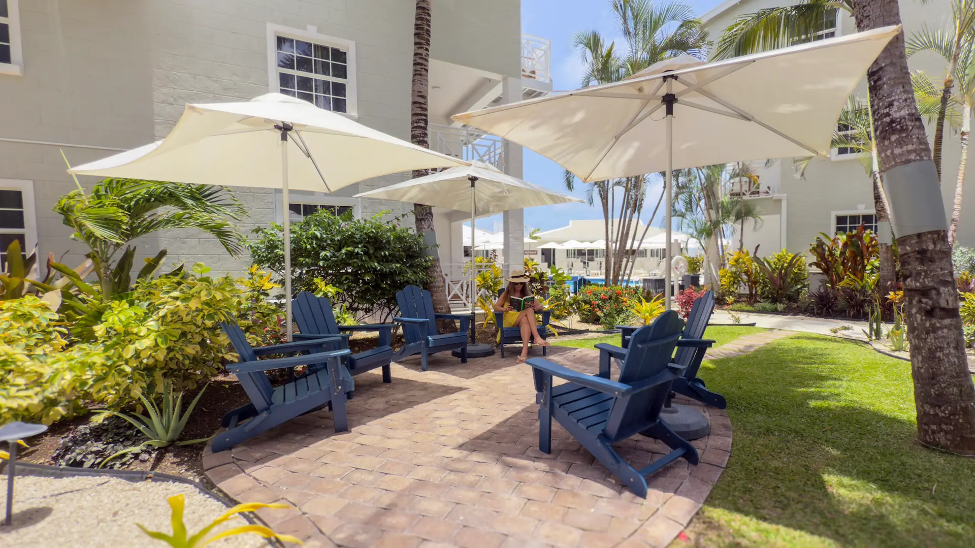 Outdoor patio area at South Point Hotel with blue lounge chairs and large umbrellas, surrounded by tropical plants, with a woman relaxing.
