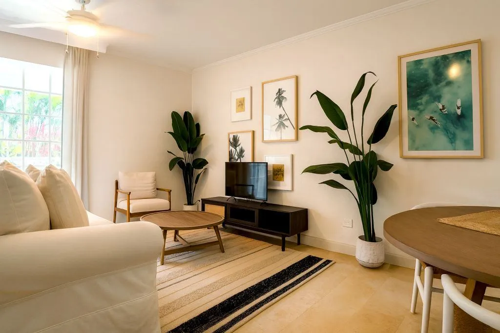 Modern tropical-style living room with natural light, neutral furniture, wood accents, large potted plants, and framed wall art, creating a warm and inviting atmosphere.