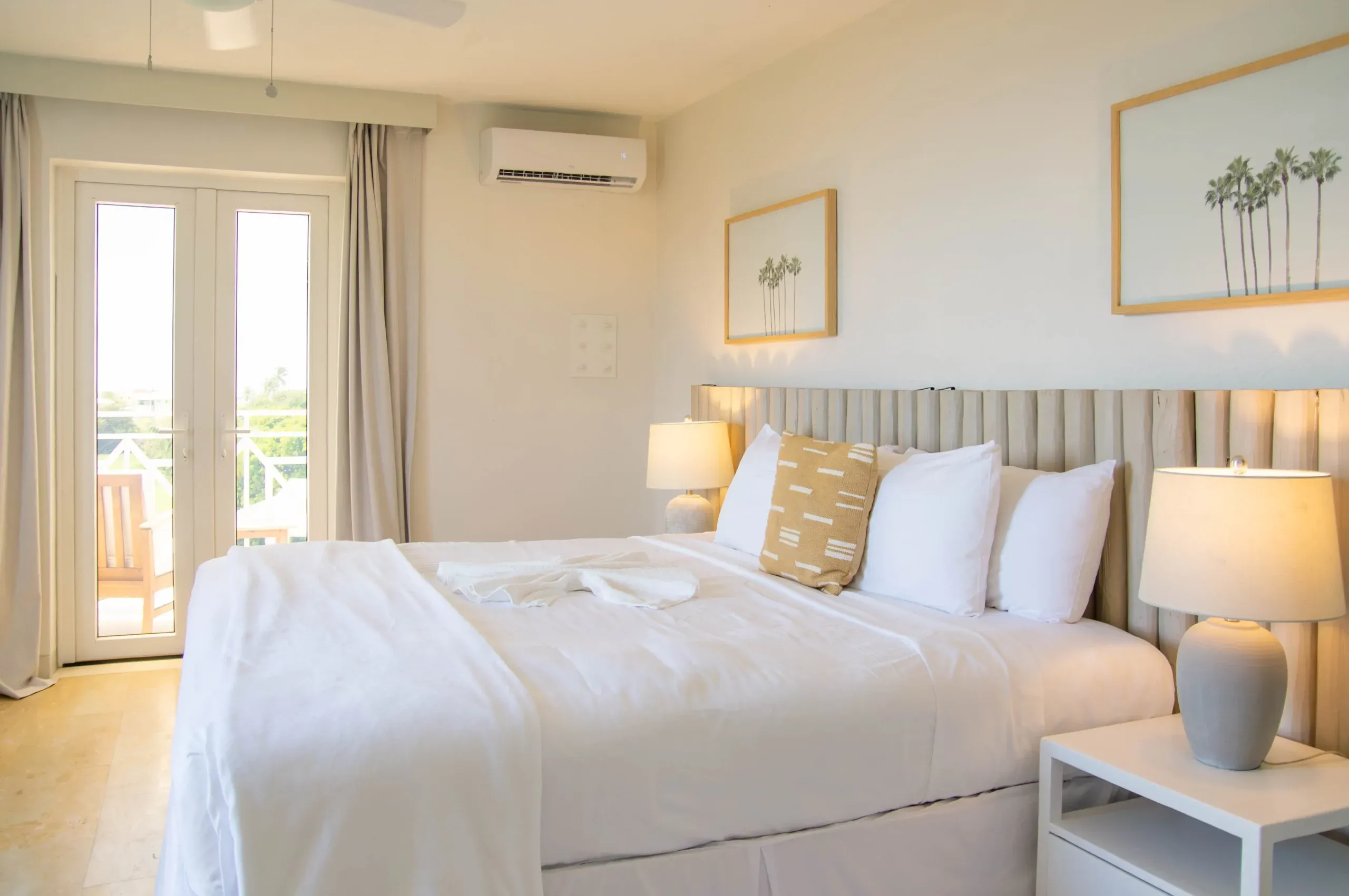The king sized bed of the King Ocean View Suite, nicely made, and decorated with yellow & cream coloured decor. The balcony overlooks the hotel grounds.