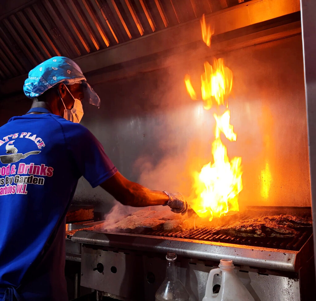 Chef in blue shirt grilling seafood over open flames at Oistins Fish Fry in Barbados kitchen