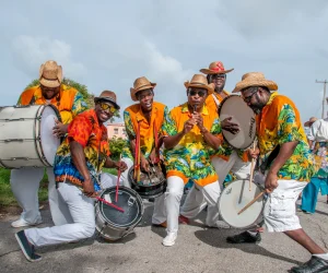 Group of Bajan musicians playing drums and percussion in colorful outfits during a street festival in Barbados