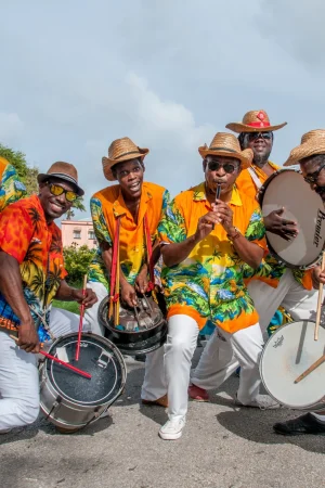 Group of Bajan musicians playing drums and percussion in colorful outfits during a street festival in Barbados