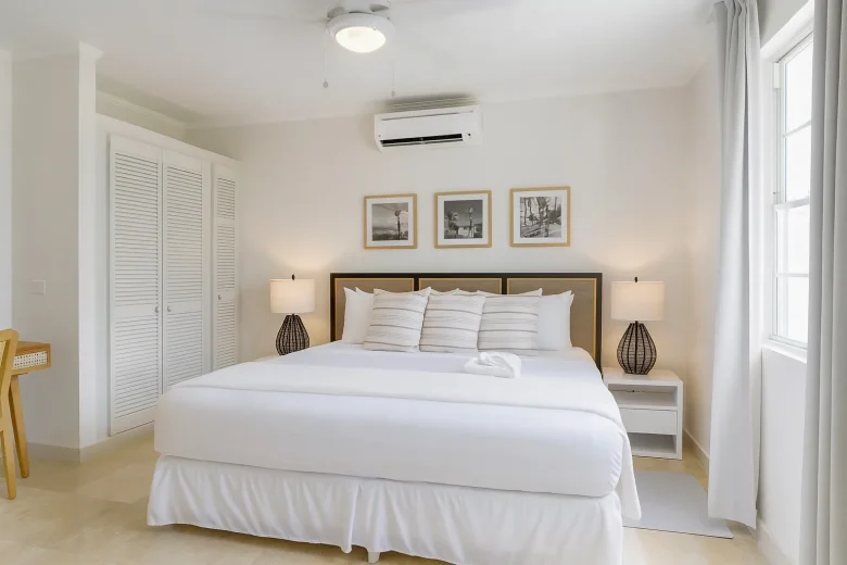 Bedroom in a presidential suite with a large neatly made bed, two bedside tables with lamps, framed artwork above the headboard, a ceiling fan, and natural light coming through a window.