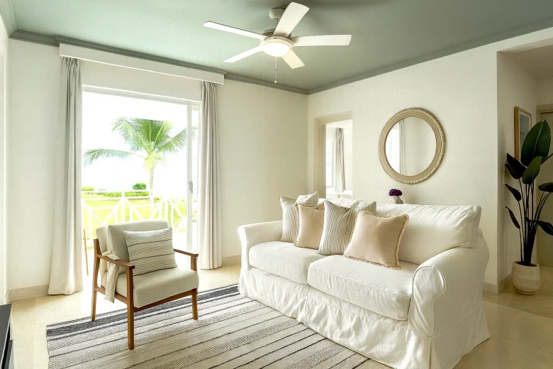 Living area in the presidential suite at South Point Hotel featuring a white sofa with cushions, an armchair, a ceiling fan, a round wall mirror, and large windows with a view of palm trees and a balcony.