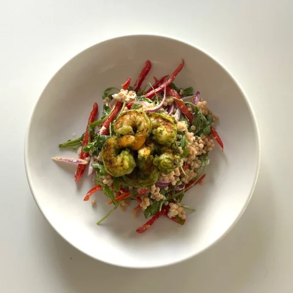 Salad featuring couscous or grains tossed with arugula, sliced red onions and peppers, and topped with herb-coated protein pieces.