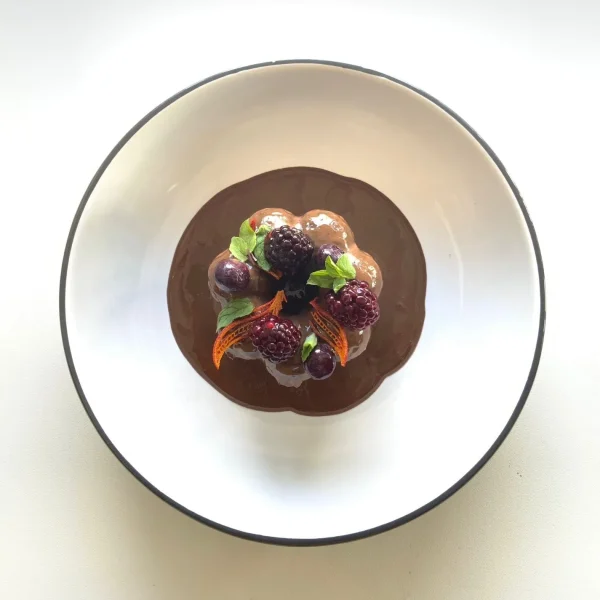 Dessert bowl of rich chocolate mousse topped with assorted berries, orange segments, and mint leaves.