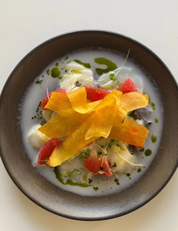 Artful dish with creamy base, green drizzle, red segments, and crispy yellow chips on top.